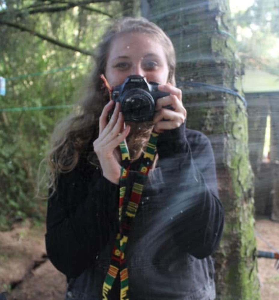 Kailee, holding a camera slightly covering her face. Taking a photo of herself in an outdoor window.